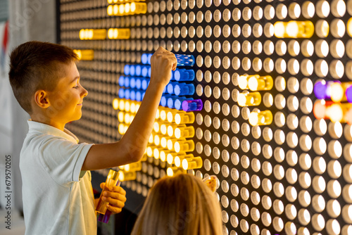 Kids making a picture with colored chips on the wall, playing on interactive models in science museum. Concept of children's entertainment and learning photo