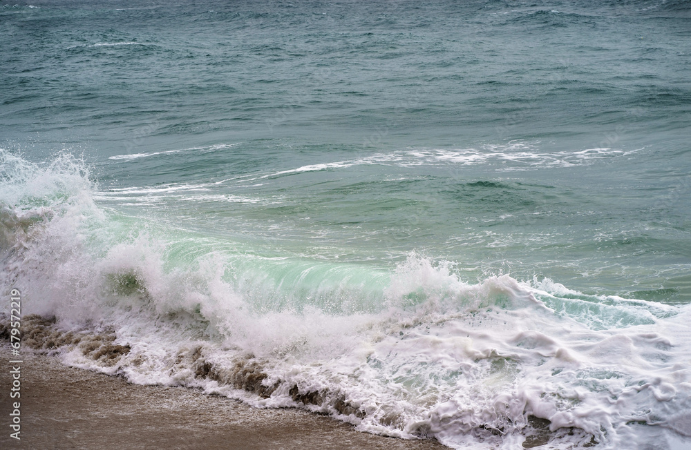 Fototapeta premium Sea element. The sea is out of season, stormy, bad weather. A sea wave breaks with white foam and splashes on the surface of the earth, sandy beach