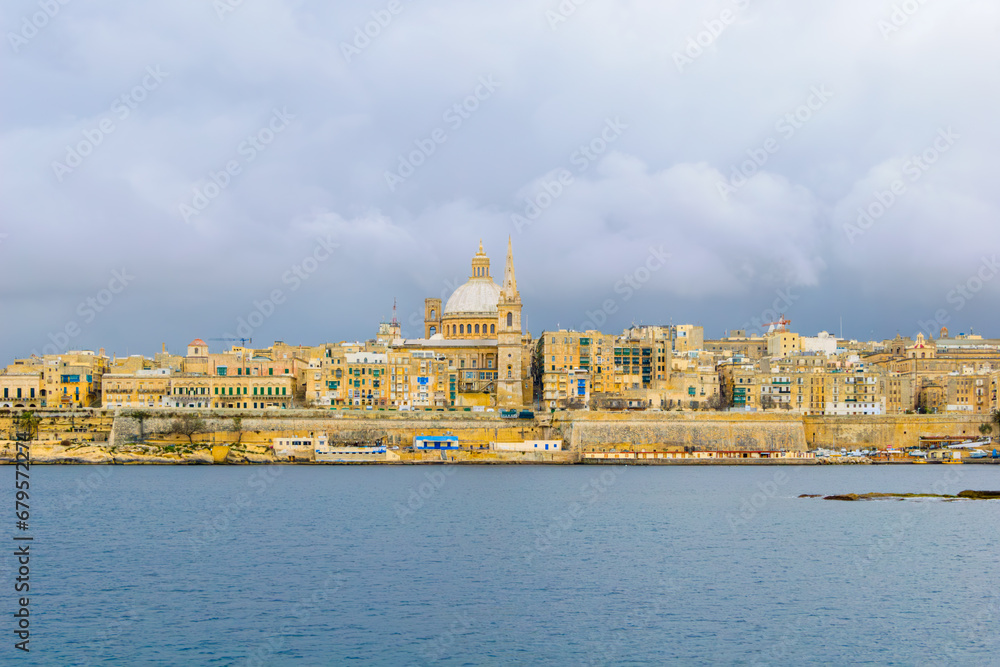 Valletta capital city under overcast sky, with Our Lady of Mount Carmel church cupola and old medieval buildings over Sliema harbor, in Malta, Mediterranean Sea