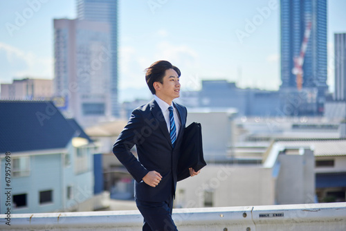 カバンを持って走るスーツを着た若い日本人ビジネスマン photo