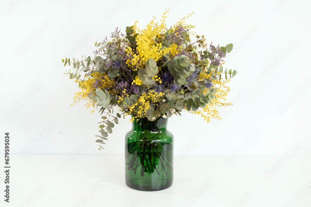 Ramo de flores mimosas con eucalipto en jarrón de cristal y fondo blanco