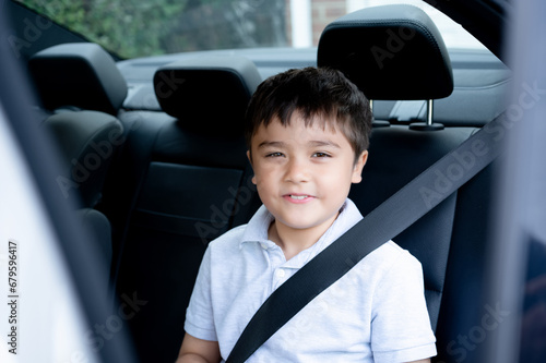 Portrait Kid Boy siting in safety car seat looking out with smiling face,Child sitting in the back passenger seat with a safety belt, School kid traveling to school by car.Back to school