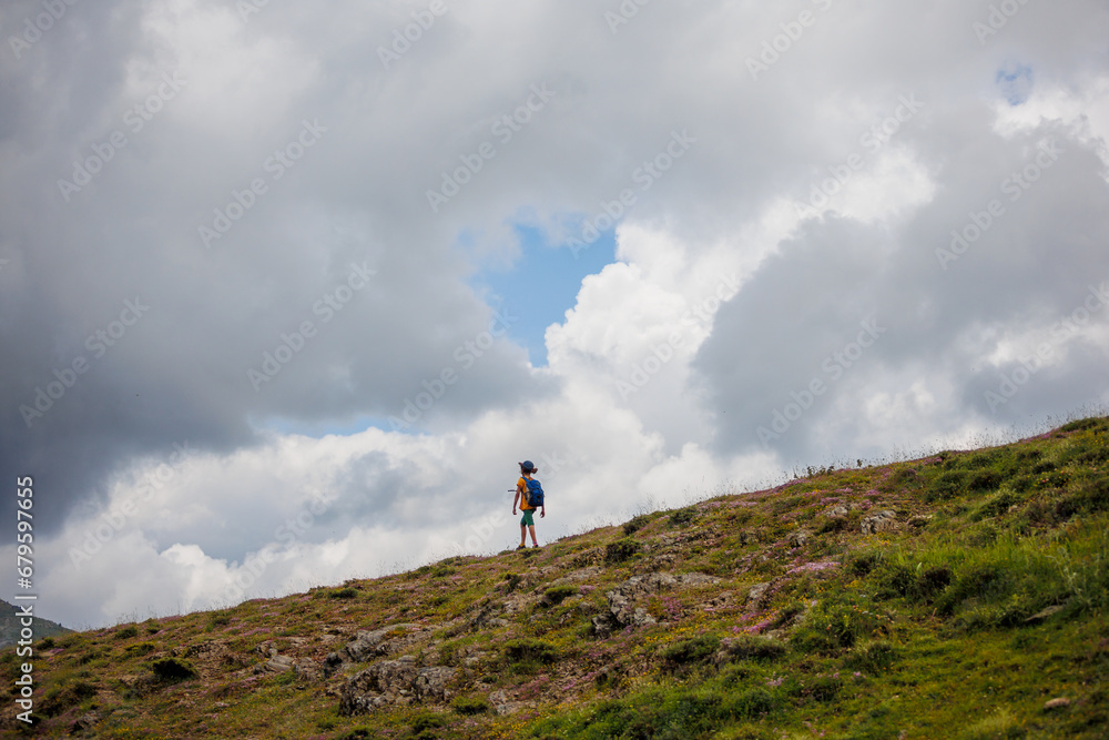 boy goes with a backpack against the backdrop of clouds in the mountains. child traveler with backpack, hiking, lifestyle concept