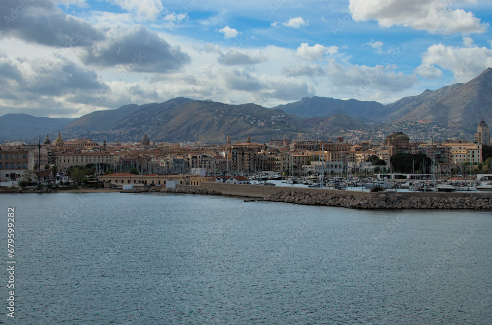 Picturesque landscape view of embankment near harbor in Palermo with moored yachts and boats. Ancient buildings in the background. Vibrant sky over mountain range. Travel and tourism concept