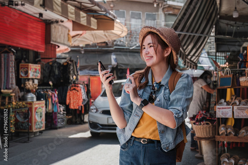 Young Asian tourist walking along city streets and holds a mobile phone on the pavement