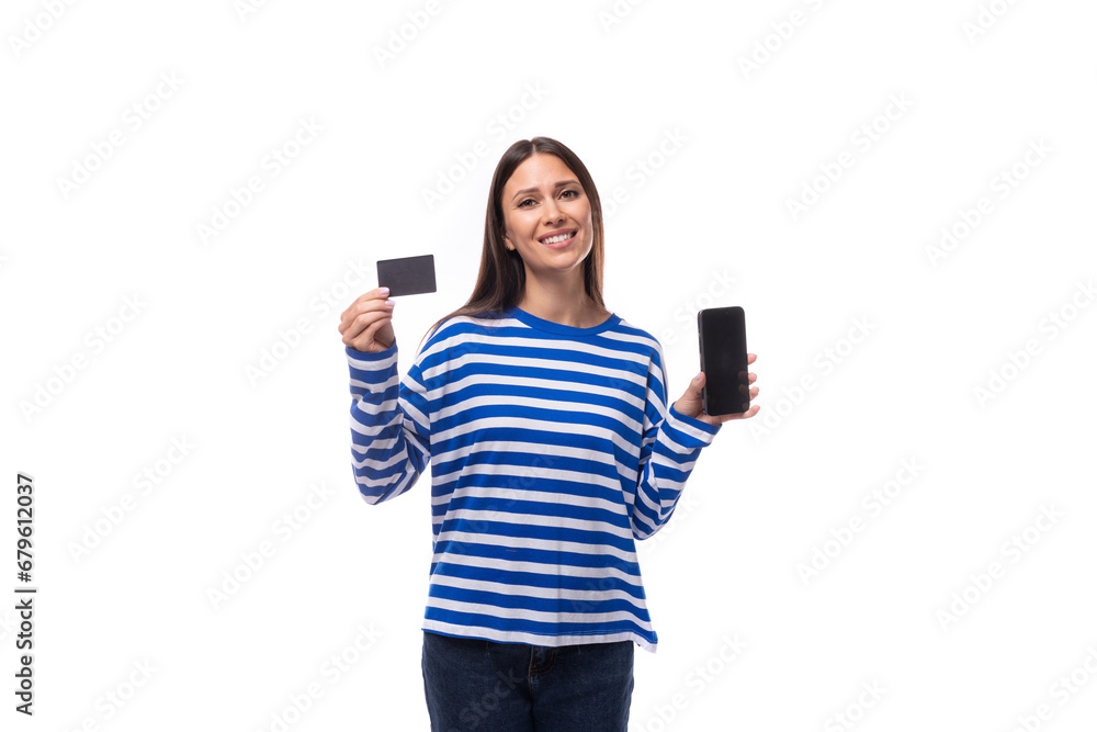 young confident european brunette woman dressed in striped blue clothes advertises bank card and smart phone young confident european brunette woman dressed in striped blue clothes advertises bank card and smart phone