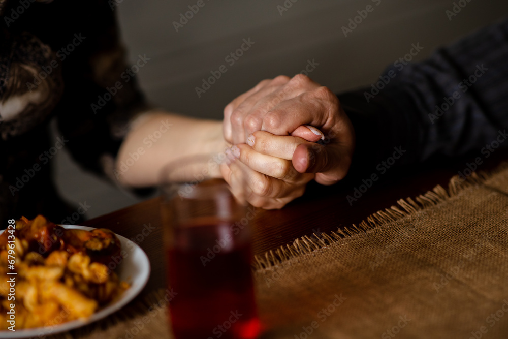 Close up shot of human hands together on table. Thanksgiving day family holding arms before having a meal. Christians people celebrate togetherness when praying at dining