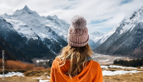 Portrait from the back of the girl traveler in an orange sweater and hat in the mountains against the background of a frozen mountain. Photo travel concept photo