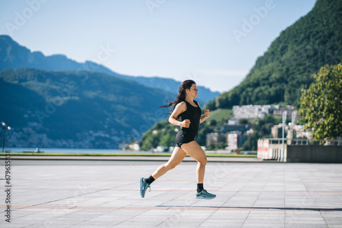 Woman trail running through alpine landscape in morning light, view of mountains behind her