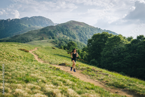 Woman trail running through alpine landscape in morning light, view of mountains behind her © SwissOutdoor