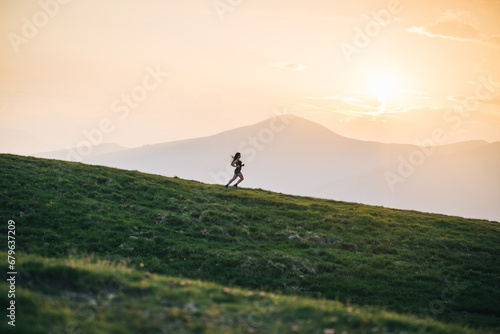 Woman trail running through alpine landscape in morning light, view of mountains behind her