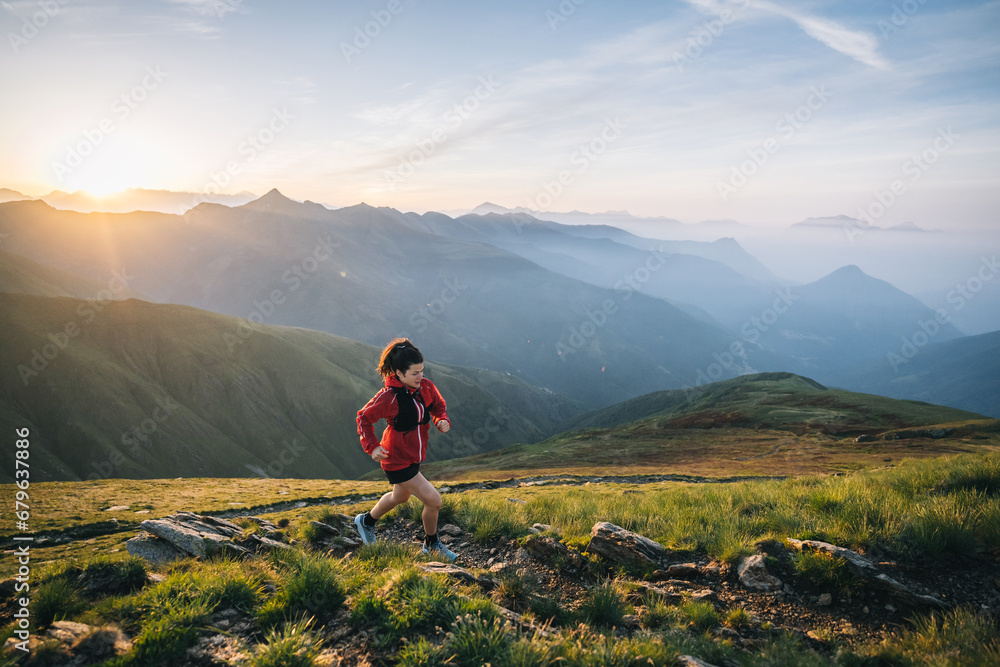 Female trail runner ascending alpine trail in the mountains at sunrise