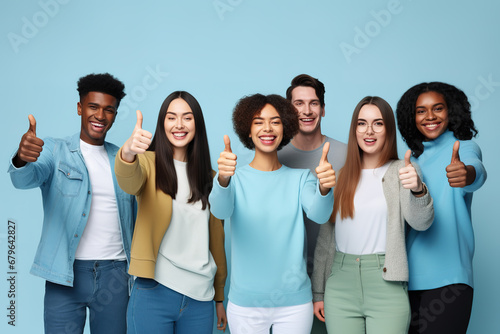 Group of young people with approving expression looking at camera showing success and like gesture on blue background. Diverse happy multiracial people holding raised thumbs ups. photo