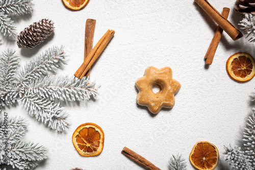 Star-shaped gingerbread on a white snowy background among cinnamon and dried orange and snow-covered branches of a Christmas tree