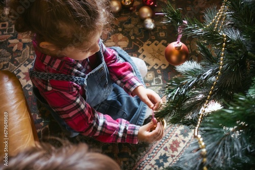 A cute little white Caucasian girl viewed from above decorating a Christmas tree with decorative baubles - high-angle view looking down photo