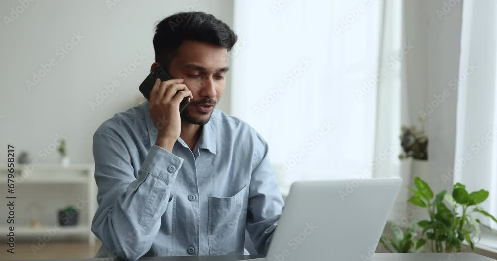 Serious busy Indian freelance professional man speaking on mobile phone at laptop, working on online startup project at home, enjoying communication, using wireless connection for job Serious busy Indian freelance professional man speaking on mobile phone at laptop, working on online startup project at home, enjoying communication, using wireless connection for job