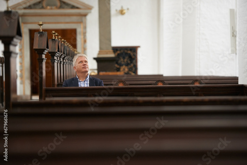Senior man, sitting and church for religion, faith or pray at cathedral or holy grounds in Jesus Christ. Mature or religious male person looking up in sanctuary for salvation, forgiveness or worship
