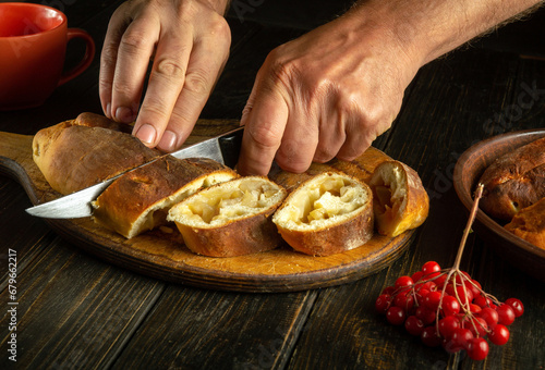 Close-up of a man hands using a knife to cut a fruit pie on a kitchen board before setting the holiday table