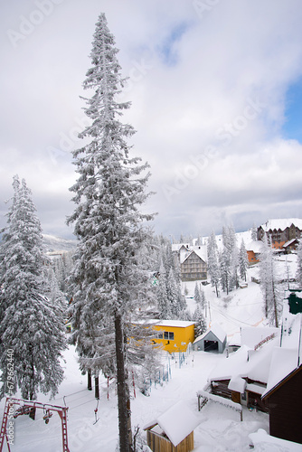 Ski resort. Winter bright snowy background. New Year's landscape with snowdrifts and pine branches in the cold. View of the rope tow, descent and Wooden houses.