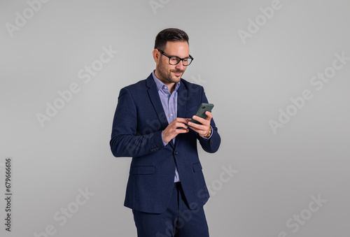 Confident young businessman text messaging over smart phone while standing on white background