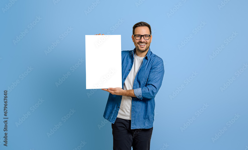 Portrait of smiling young businessman showing blank placard for advertising on blue background Portrait of smiling young businessman showing blank placard for advertising on blue background