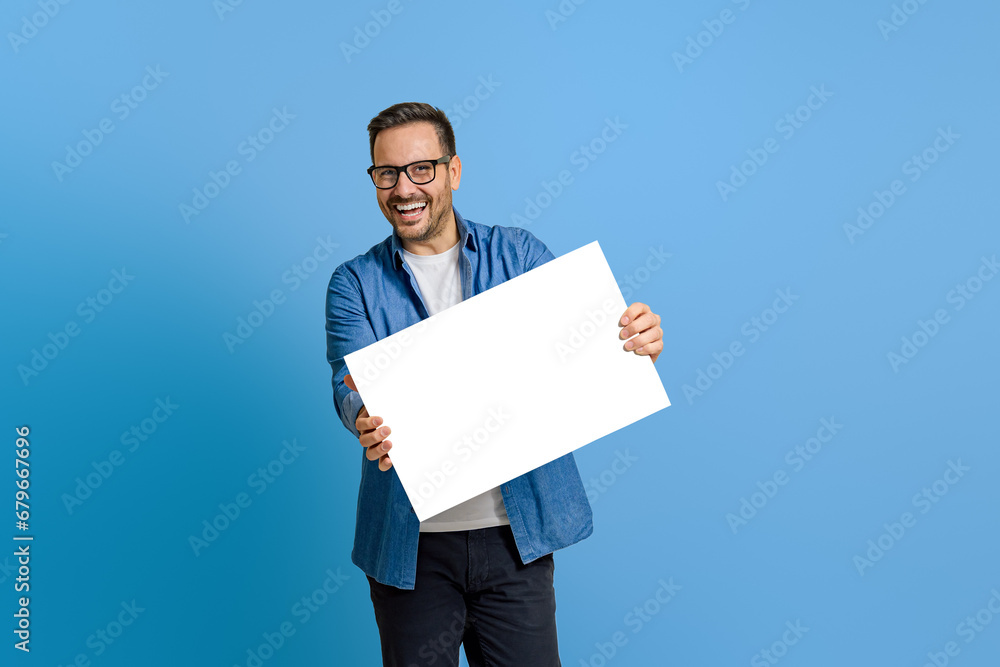 Portrait of cheerful marketing manager showing blank white banner while standing on blue background Portrait of cheerful marketing manager showing blank white banner while standing on blue background