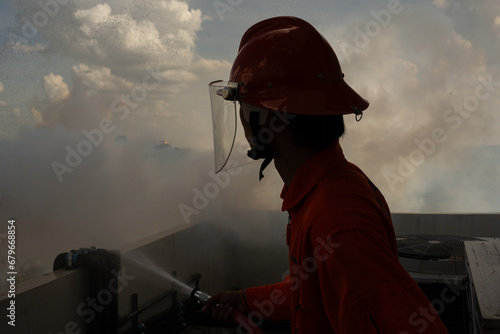 Silhouette firefighter holding water hose and water spraying to prevent high building.Fire fighting training.Fire man spray high pressure water to fire.Fire fighting concept.