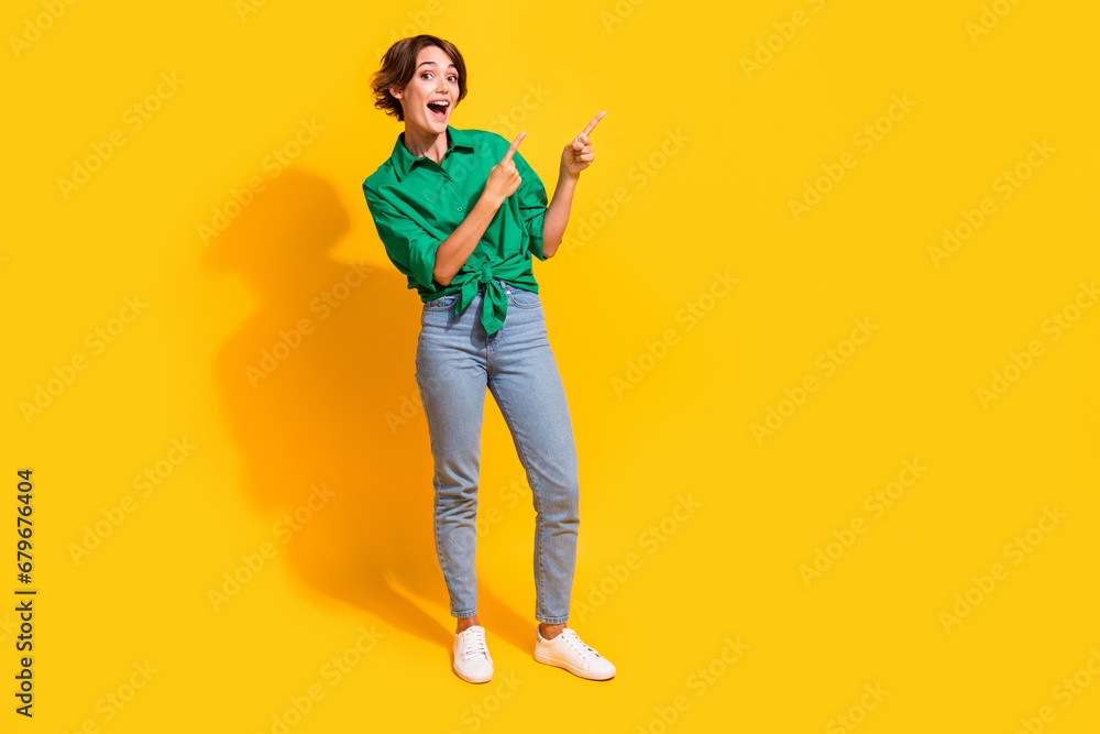 Fototapeta premium Full length photo of funky excited girl dressed green shirt pointing two fingers empty space isolated yellow color background