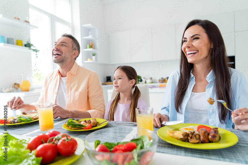 Photo of charming funny married couple small daughter laughing enjoying delicious dinner indoors home kitchen
