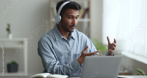 Serious freelance project manager man talking to business partner on video call, using wireless headphones and laptop for job communication, online conference connection, working from home photo