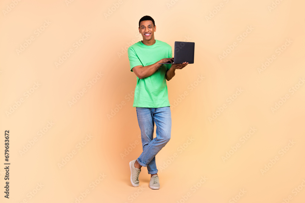 Full length photo of handsome good mood man wear stylish t-shirt jeans holding laptop write email isolated on beige color background Full length photo of handsome good mood man wear stylish t-shirt jeans holding laptop write email isolated on beige color background