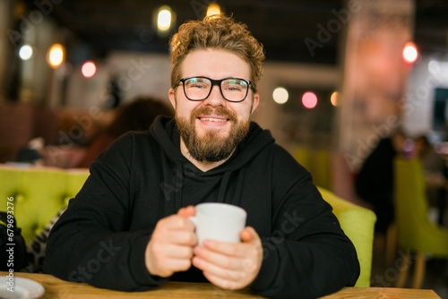 Bearded curly man smiling confident drinking coffee in restaurant or coffee shop. Millennial generation and Gen Y
