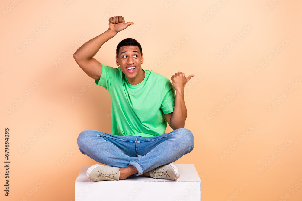 Photo of impressed funny guy dressed green t-shirt sit on platform look indicating at sale empty space isolated on beige color background Photo of impressed funny guy dressed green t-shirt sit on platform look indicating at sale empty space isolated on beige color background