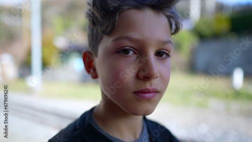 Fotografie Serious young boy close-up face looking at camera standing outside