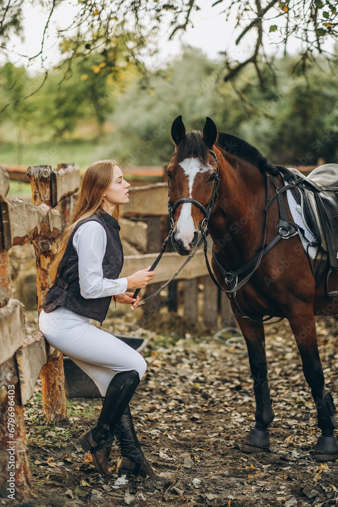 Obraz premium A young female equestrian stands near her horse and prepares for a competition.