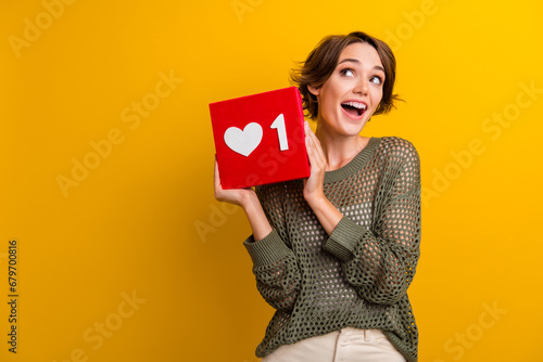 Photo of adorable excited girl hand hold red poster instagram facebook like empty space isolated on yellow color background