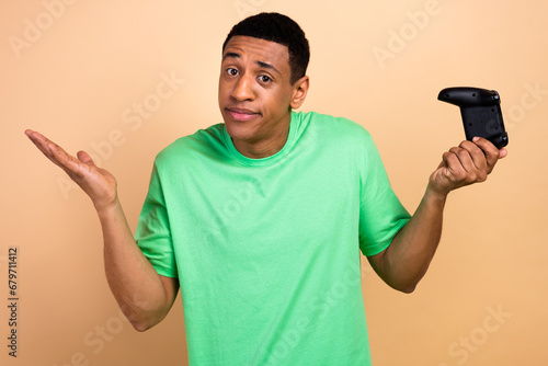 Photo portrait of attractive young man shrug shoulders playstation dressed stylish green clothes isolated on beige color background