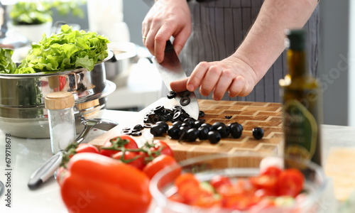 Male Hands Chopping Round Black Olives Slices. Chef Cutting Fresh Vegetable Ingredient on Wooden Board with Knife. Male Cooking Dieting Salad. Culinary Vegetarian Recipe Horizontal Photography