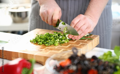 Chef Hands Holding Knife Cutting Green Onion. Man Chopping Scallion with Sharp Knife on Wooden Board at Kitchen. Fresh Greens for Dieting Cooking. Healthy Home Culinary Horizontal Photography