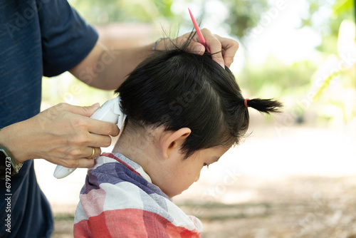 Barber cutting hair of an Asian boy In an open space filled with trees.