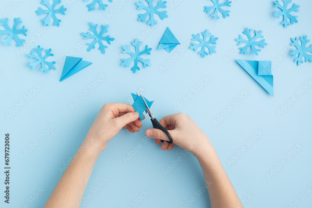 Hands making paper snowflakes on blue child hands
