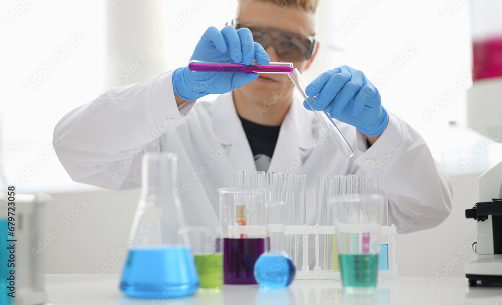 A male chemist holds test tube of glass in his hand overflows a liquid solution of potassium permanganate. Conducts an analysis reaction takes various versions of reagents using chemical manufacturing A male chemist holds test tube of glass in his hand overflows a liquid solution of potassium permanganate. Conducts an analysis reaction takes various versions of reagents using chemical manufacturing