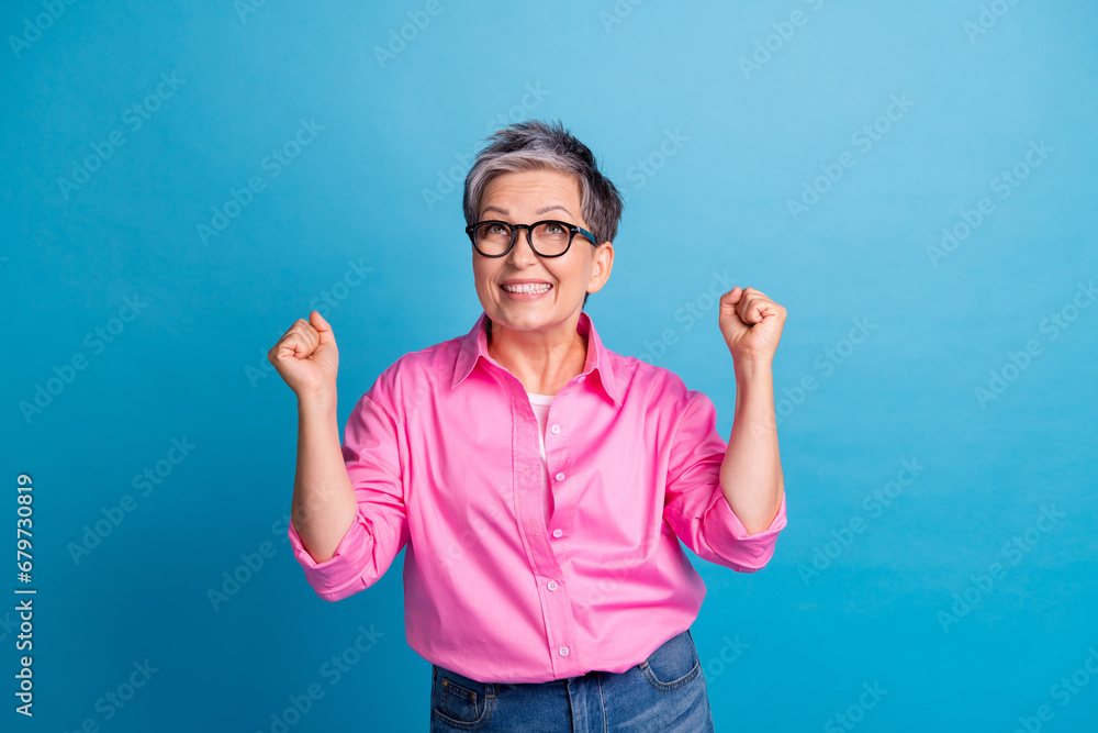 Photo of overjoyed woman with short hair dressed pink shirt look empty space win lottery raising fists isolated on blue color background Photo of overjoyed woman with short hair dressed pink shirt look empty space win lottery raising fists isolated on blue color background