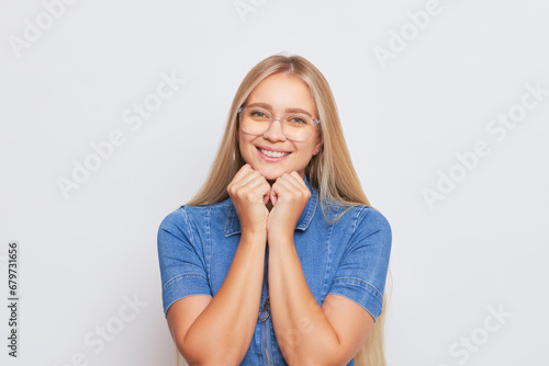 Lovely blonde girl with glasses wearing blue denim dress smiling gently isolated on background, happy life concept, copy space