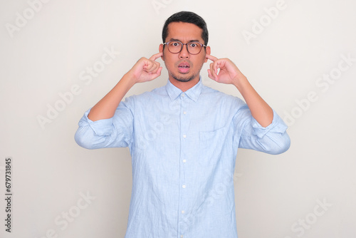 Adult Asian man closing both ears with finger with annoyed expression photo