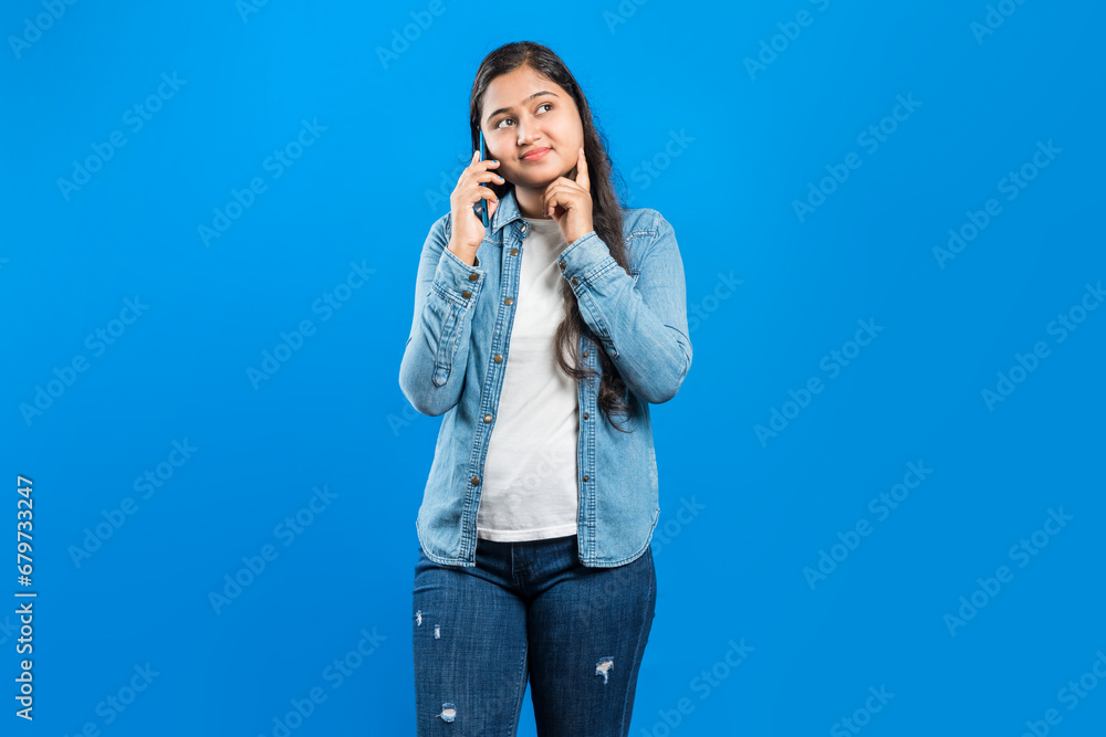 Isolated on blue background happy asian girl touching her chin, engaged in a phone call on smart phone and thinking Isolated on blue background happy asian girl touching her chin, engaged in a phone call on smart phone and thinking