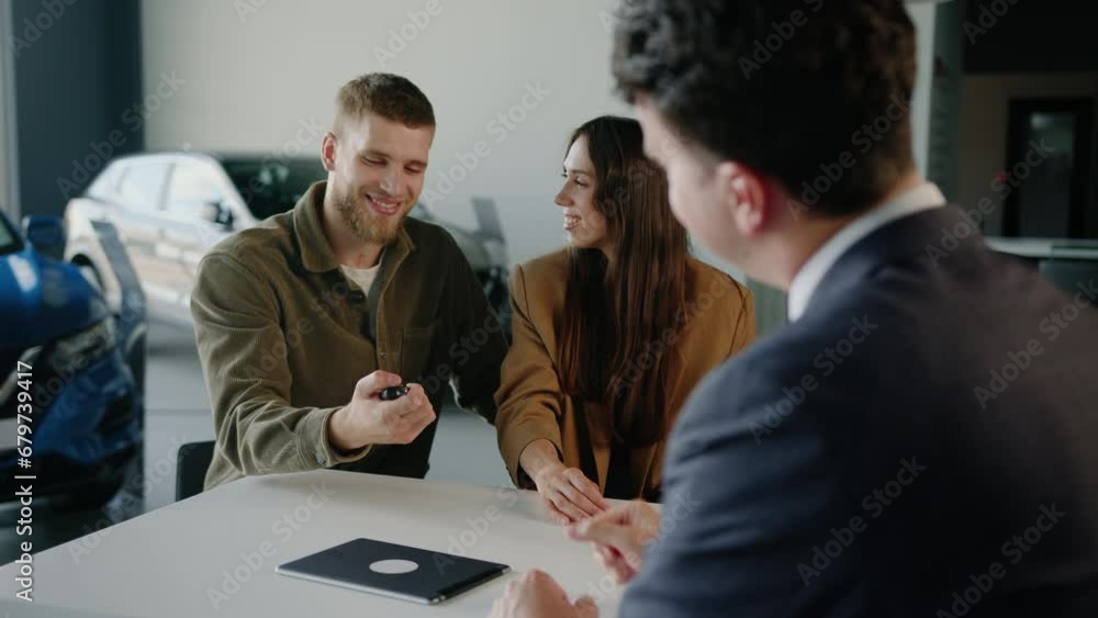 A happy young couple receives the long-awaited car keys. Buying a family car at a dealership