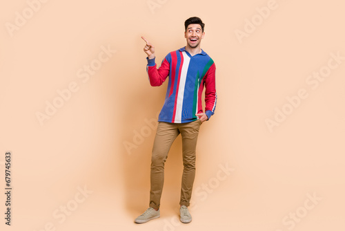 Full length photo of young man wear stylish gucci shirt and directing finger looking empty space excited isolated on beige color background