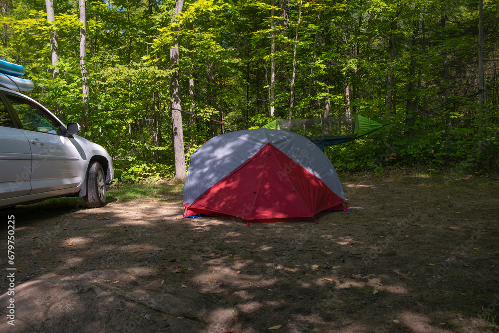 Set up campsite in the forest - tent with hanging hammock and parked SUV truck with inflated paddle boards on the roof in the background. Summer vacation, adventure, road trip concept. Set up campsite in the forest - tent with hanging hammock and parked SUV truck with inflated paddle boards on the roof in the background. Summer vacation, adventure, road trip concept.