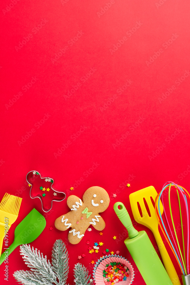 Obraz premium Creating festive delicacies concept. Top view composition of cute cookies, candies, pastry tools, baking tins, frosty fir twig, stars on red background with advert zone